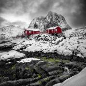 Winter landscape in Hamnøy, Norway, with rocks covered in green moss and red cabins contrasting with the snow and grey sky