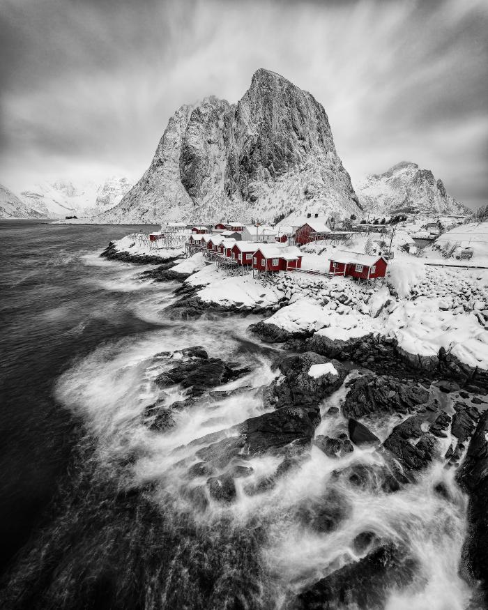 Winter view of Hamnøy in the Lofoten Islands, with rough sea, snow on the rocks, and red cabins standing out beneath a snowy mountain