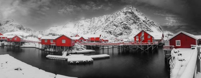 Winter panorama of Å, the last village in Lofoten, with red cabins facing the icy sea and snowy mountains in the background